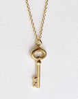 Image is a 24K gold plated key charm pendant delicate necklace, handmade by Izaskun Zabala.