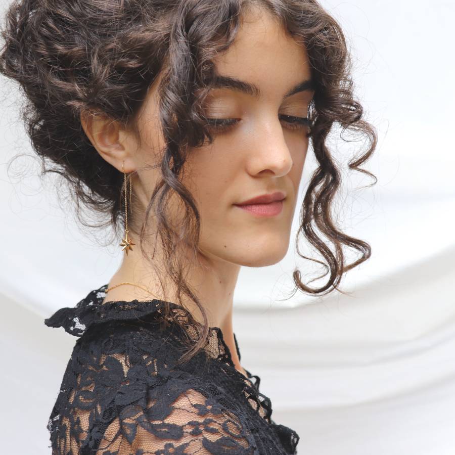 Image is a model wearing a pair of 24K gold plated dangling star earrings with a tiny black spinel, handmade by Izaskun Zabala.