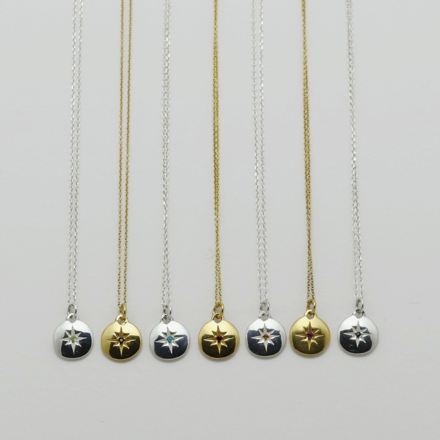 Image is a selection of zodiac necklaces in silver and gold-plate, with a small medallion pendant and star engraved birthstone, handmade by Izaskun Zabala.
