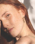 Image is a pair of earrings of a woman's figure dangling from a shell stud, handmade by Izaskun Zabala.