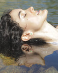 Model lying on water with reflection, wearing an emerald hexagon stud earring, handmade by Izaskun Zabala.