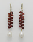 Pair of earrings with briolette garnets and pearl drops on a light gray background, handmade by Izaskun Zabala.