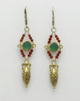 Pair of golden drop amphora earrings with green gemstones and red beads on a white background, handmade by Izaskun Zabala.