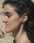 Close-up of a woman wearing a golden floral climber earring, handmade by Izaskun Zabala, with a blurred natural background.