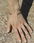 Hand with a golden snake-shaped bangle handmade by Izaskun Zabala, on a textured stone surface.