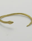 Golden snake-shaped bangle with garnet eyes handmade by Izaskun Zabala, on a light gray background.