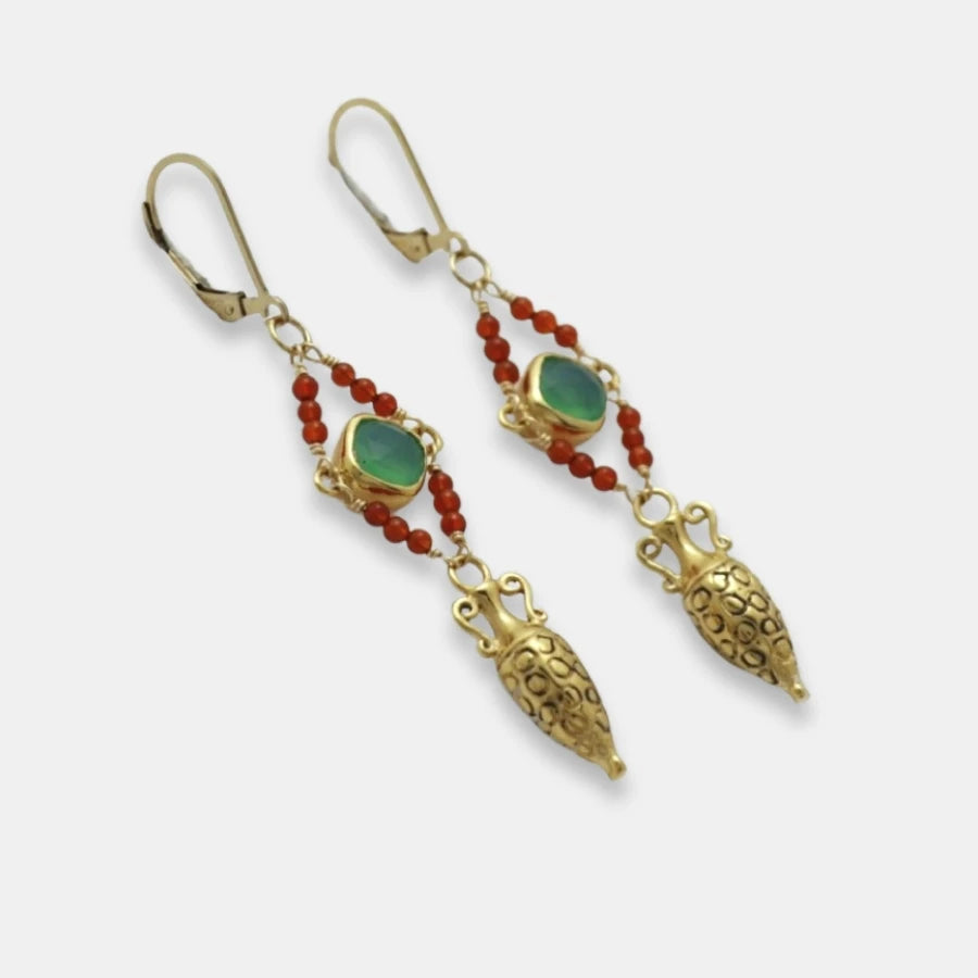 Side view of golden drop amphora earrings with green gemstones and red beads on a white background, handmade by Izaskun Zabala.