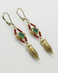 Pair of golden drop amphora earrings with green gemstones and red beads on a white background, handmade by Izaskun Zabala.