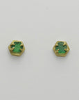 Pair of green emerald stud earrings with golden hexagonal settings on a light gray background, handmade by Izaskun Zabala.