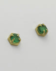 Pair of green emerald stud earrings with golden hexagonal settings on a light gray background, handmade by Izaskun Zabala.