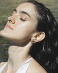 Woman with wet hair wearing a golden mermaid stud earring against a water background, handmade by Izaskun Zabala.