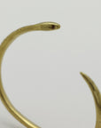 Golden snake-shaped bangle with garnet eyes handmade by Izaskun Zabala, on a light gray background.