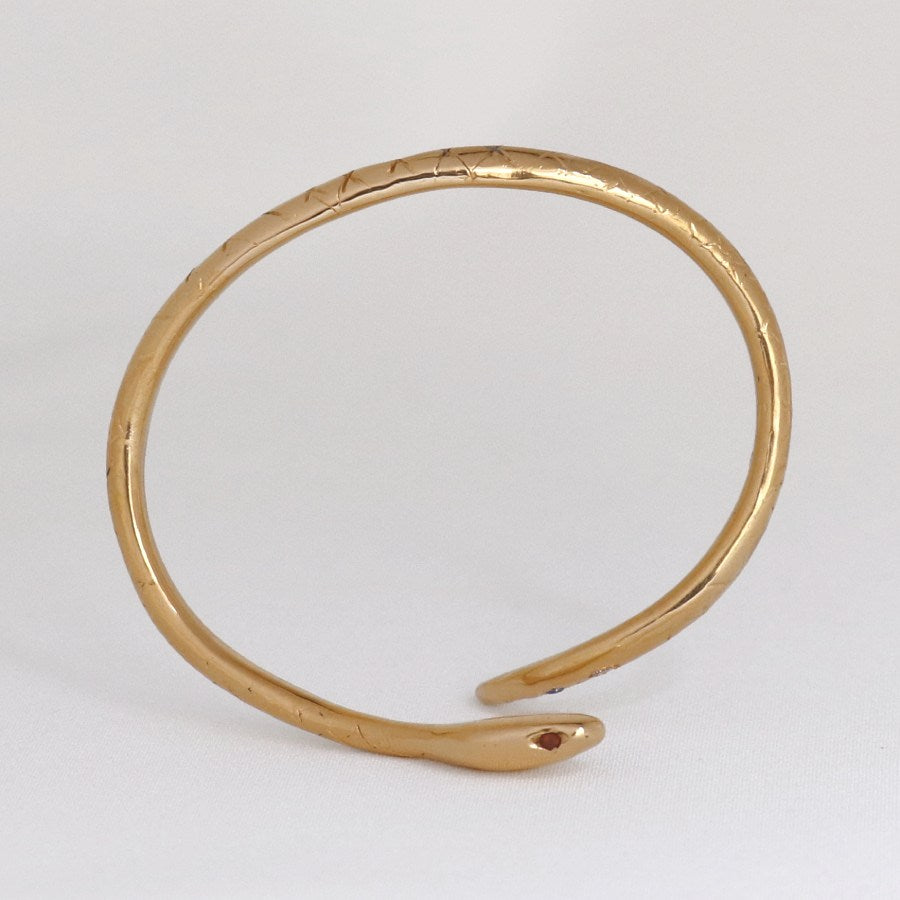 Image is a 24K gold plated snake cuff with garnet eyes, tanzanite and white topaz stones, handmade by Izaskun Zabala.