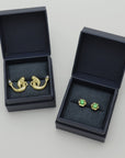 Two pairs of golden unique earrings in dark blue Izaskun Zabala branded boxes on a light gray background.
