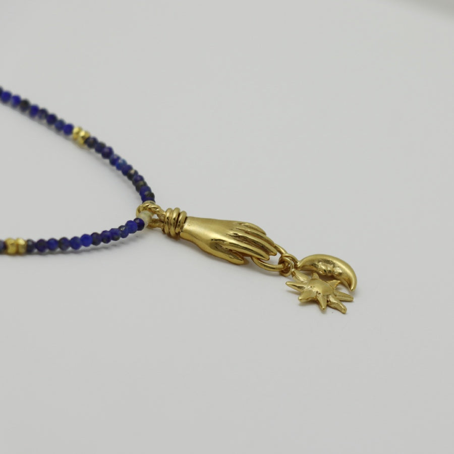 Image is a lapis lazuli beaded chain with a gold-plated miniature hand pendant and removable sun and moon charms, handmade by Izaskun Zabala.