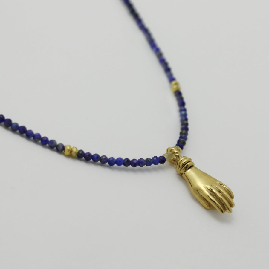 Image is a lapis lazuli beaded chain with a gold-plated miniature hand pendant, handmade by Izaskun Zabala.
