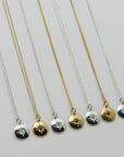 Image is a selection of zodiac necklaces in silver and gold-plate, with a small medallion pendant and star engraved birthstone, handmade by Izaskun Zabala.