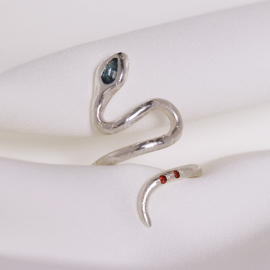 Image is a silver snake ring with a pear shape london topaz and two garnets in the tail, handmade by Izaskun Zabala.