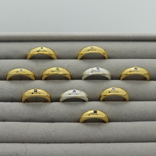 Gold plated and silver rings with an engraved star and gemstones, handmade by Izaskun Zabala, on a gray cushioned display.