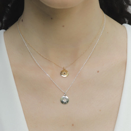 Image is a pair of silver and gold-plate necklaces with a small medallion pendant and star engraved birthstone on model, handmade by Izaskun Zabala.