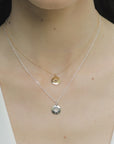 Image is a pair of silver and gold-plate necklaces with a small medallion pendant and star engraved birthstone on model, handmade by Izaskun Zabala.