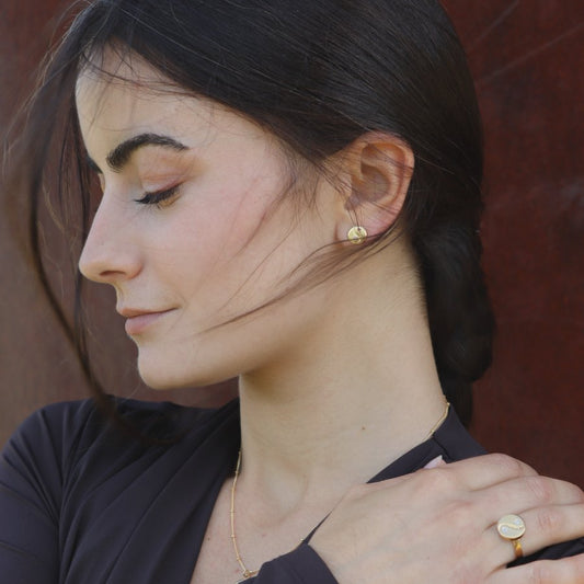 Close-up of a woman wearing gold-plated yin yang earrings and ring, artisan made by Izaskun Zabala.