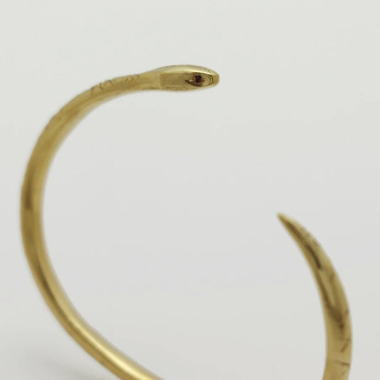 Detail of 24K gold-plated snake-shaped bangle with garnet eyes, handmade by Izaskun Zabala.