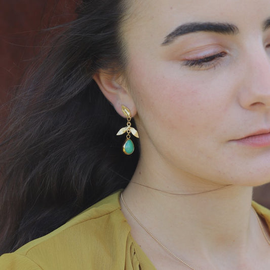 Close-up of a woman wearing gold-plated leaf earrings with green teardrop stone.
