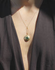 Gold-plated necklace with a green pendulum pendant on a woman wearing a dark brown top.