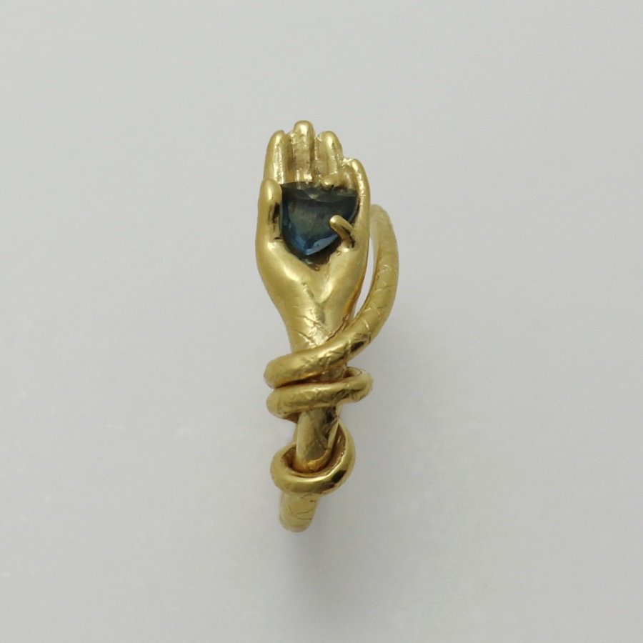 Image is a 24K gold-plated snake like band with a hand holding a topaz ring, handmade by Izaskun Zabala.