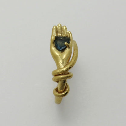 Image is a 24K gold-plated snake like band with a hand holding a topaz ring, handmade by Izaskun Zabala.