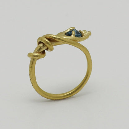 Image is a 24K gold-plated snake like band with a hand holding a topaz ring, handmade by Izaskun Zabala.