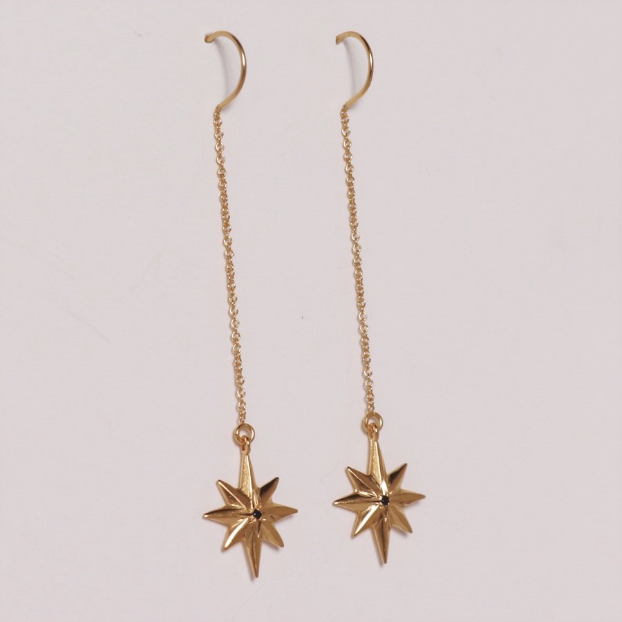 Image is a pair of 24K gold plated dangling star with a tiny black spinel earrings, handmade by Izaskun Zabala.