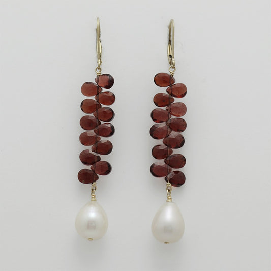 Pair of earrings with briolette garnets and pearl drops on a light gray background, handmade by Izaskun  Zabala.