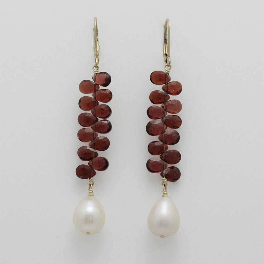 Pair of earrings with briolette garnets and pearl drops on a light gray background, handmade by Izaskun  Zabala.