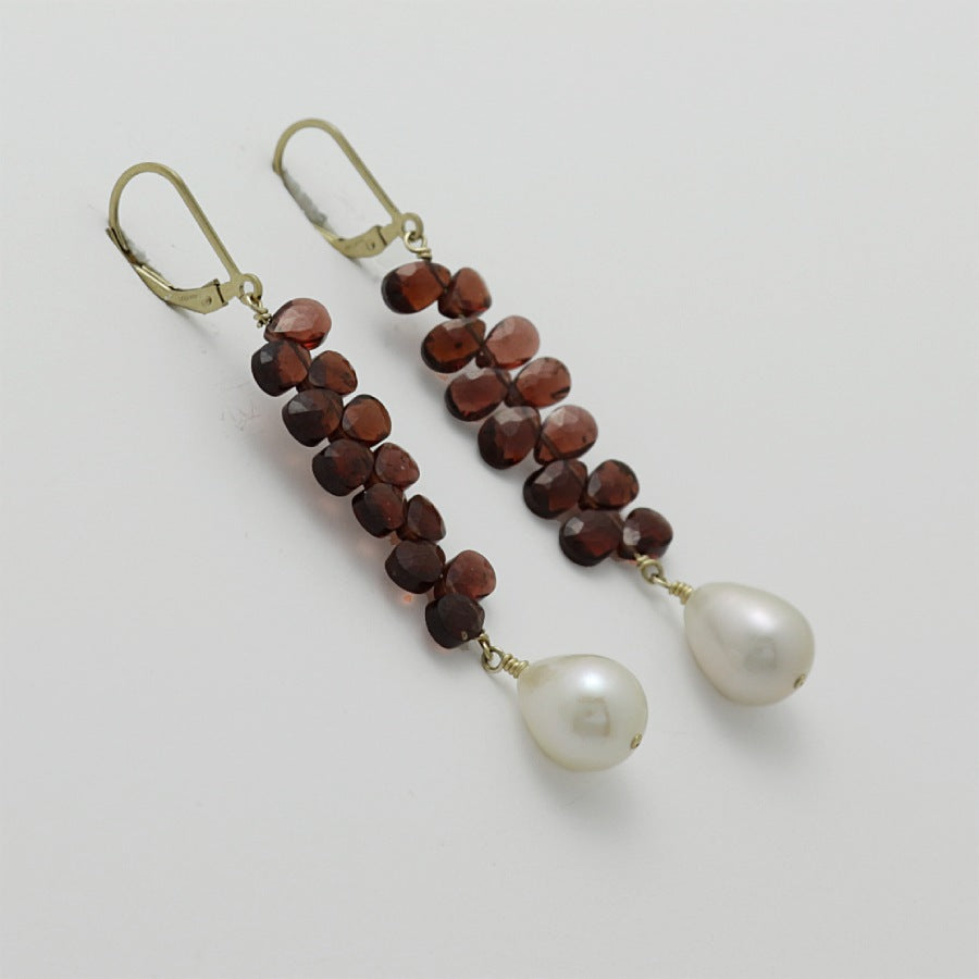 Pair of earrings with briolette garnets and pearl drops on a light gray background, handmade by Izaskun  Zabala.