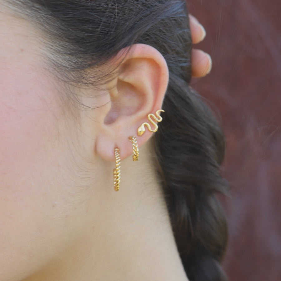 Close-up of a woman wearing gold-plated hoop earrings and snake stud, handmade by Izaskun Zabala.