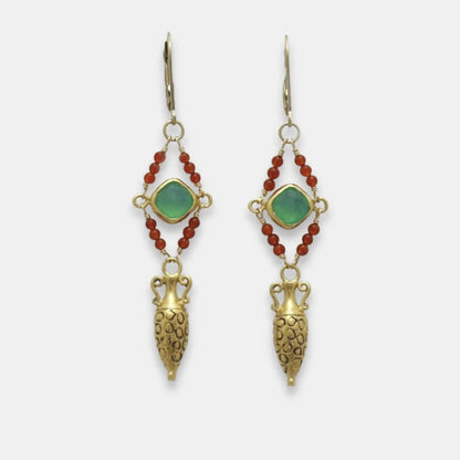 Pair of golden drop amphora earrings with green gemstones and red beads on a white background, handmade by Izaskun Zabala.