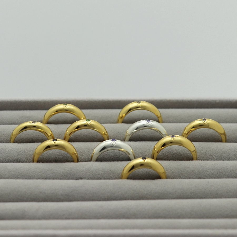Gold plated and silver rings with an engraved star and gemstones, handmade by Izaskun Zabala, on a gray cushioned display.