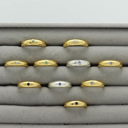 Gold plated and silver rings with an engraved star and gemstones, handmade by Izaskun Zabala, on a gray cushioned display.