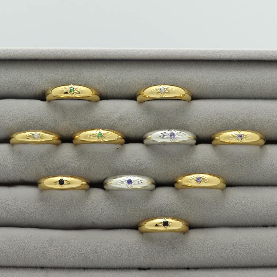 Gold plated and silver rings with an engraved star and gemstones, handmade by Izaskun Zabala, on a gray cushioned display.