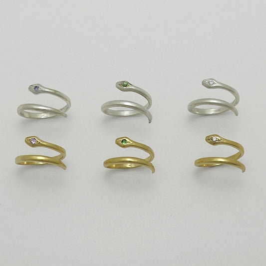 Set of snake-shaped gold plated and silver rings with gemstones on a light gray background, handmade by Izaskun Zabala.