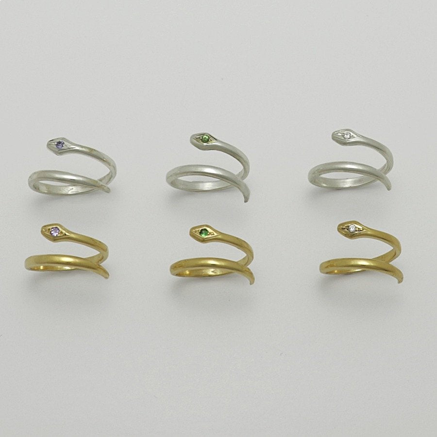 Set of snake-shaped gold plated and silver rings with gemstones on a light gray background, handmade by Izaskun Zabala.