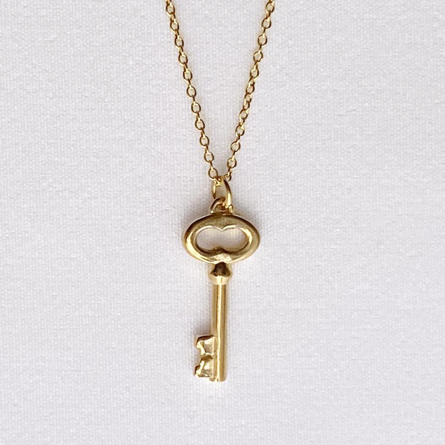 Image is a golden key charm pendant delicate necklace, handmade by Izaskun Zabala.