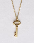 Image is a golden key charm pendant delicate necklace, handmade by Izaskun Zabala.