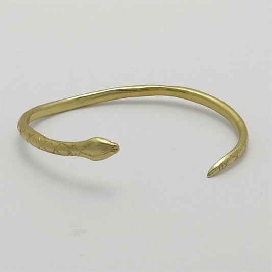 Golden snake-shaped bangle with garnet eyes handmade by Izaskun Zabala, on a light gray background.