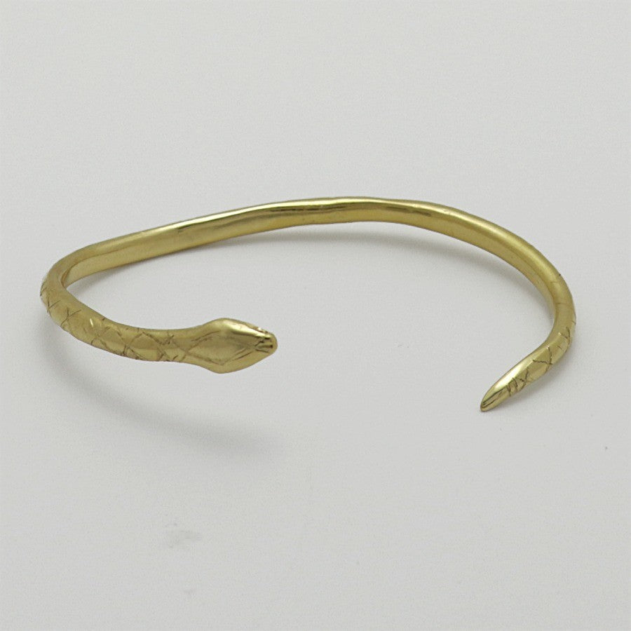 Golden snake-shaped bangle with garnet eyes handmade by Izaskun Zabala, on a light gray background.