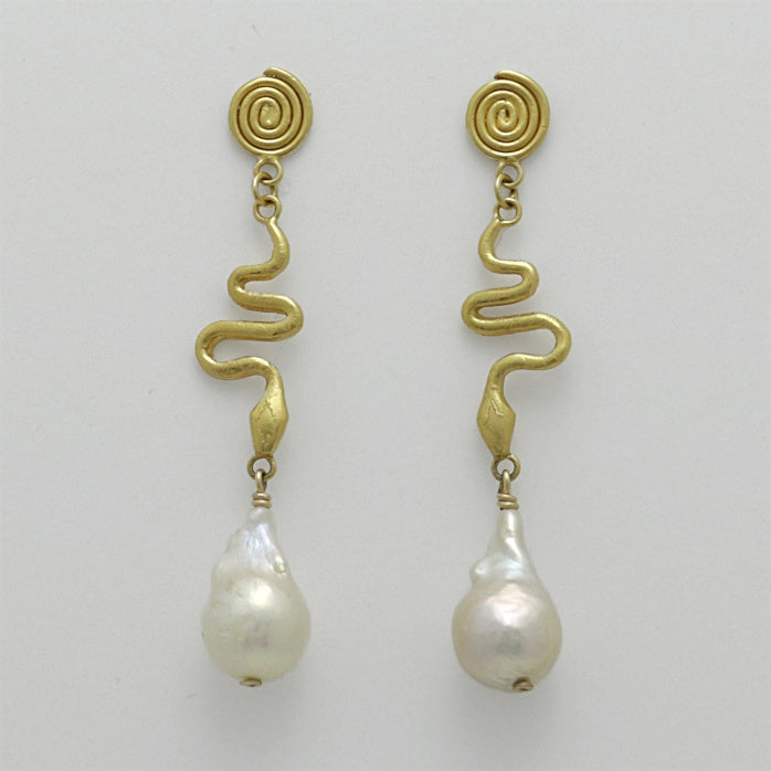 Pair of golden spiral earrings with baroque pearl drops, handmade by Izaskun Zabala, on a light gray background.