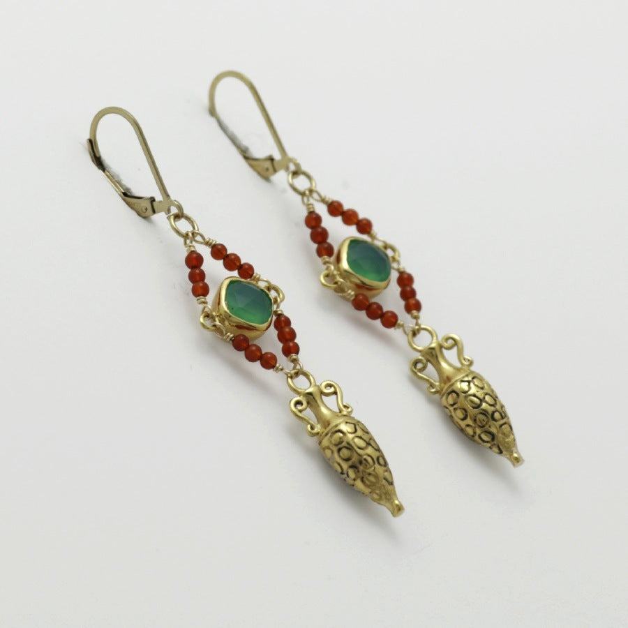 Pair of golden drop amphora earrings with green gemstones and red beads on a white background, handmade by Izaskun Zabala.