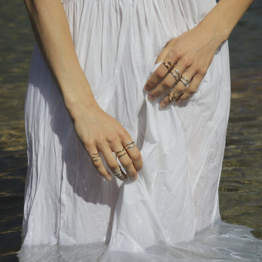 Model wearing a white dress with multiple handmade snake rings by Izaskun Zabala, standing in water.